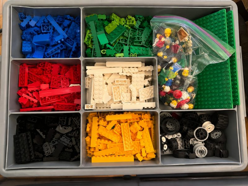 Photo of a storage bin of LEGO bricks sorted by colour with minifigures and baseplates